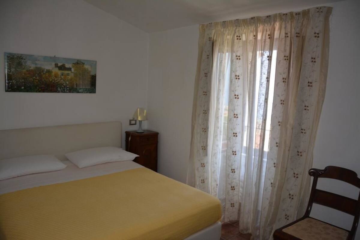 A bedroom with a bed, a nightstand, a chair, and a painting on the wall.