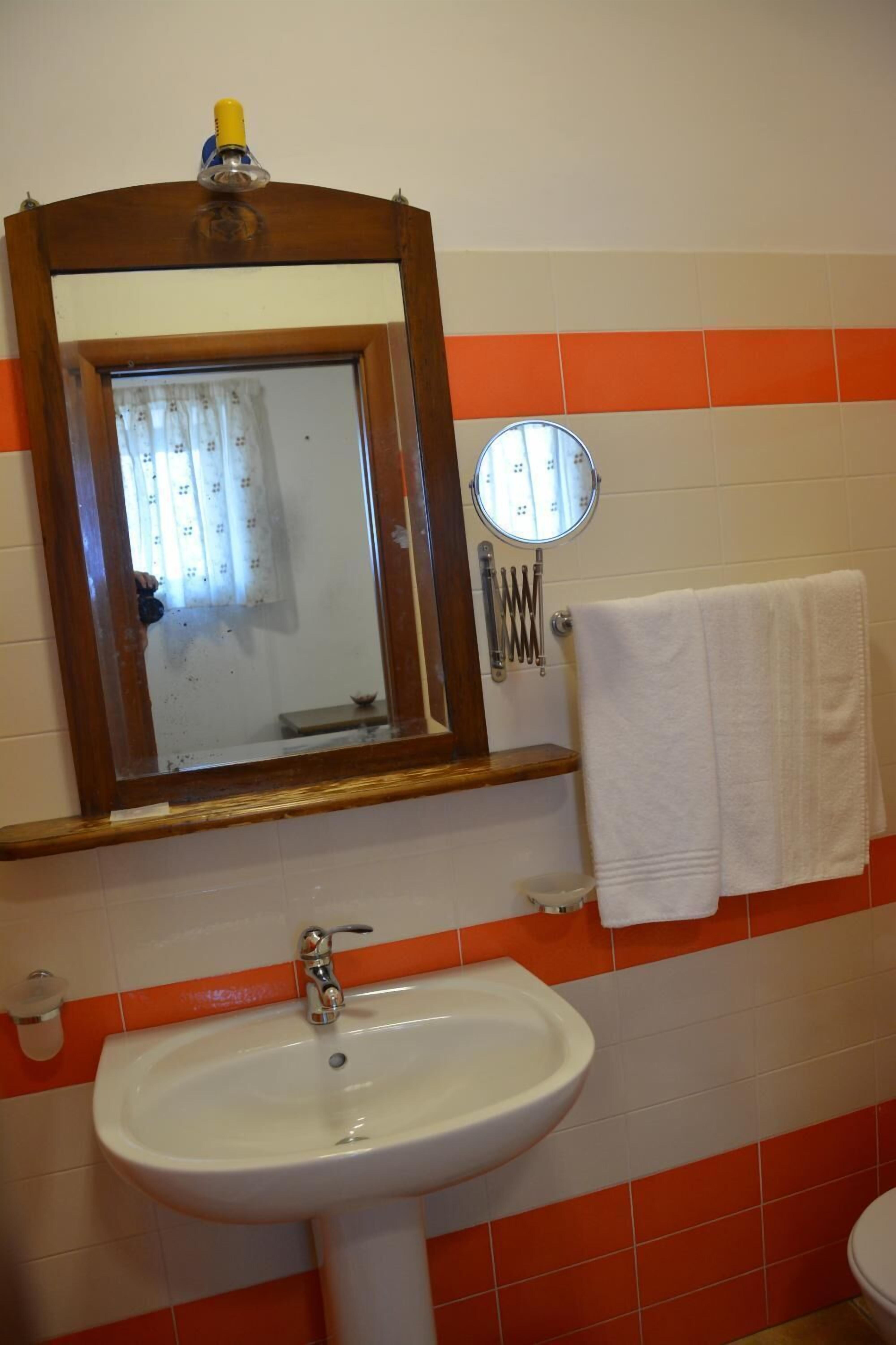 A bathroom with a white sink, a wooden-framed mirror, and an orange-tiled wall.