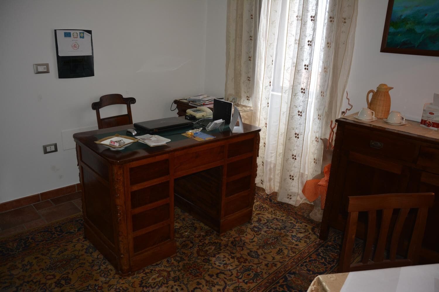 A room with a wooden desk, a chair, a small table with a pitcher, and a patterned rug.