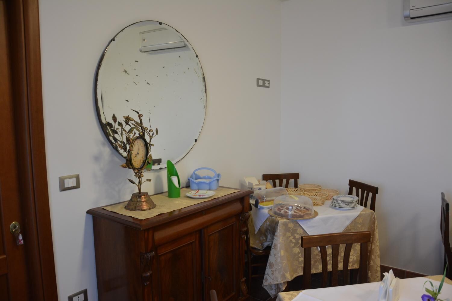 A dining area with a wooden table, chairs, a large mirror, and a clock on a cabinet.