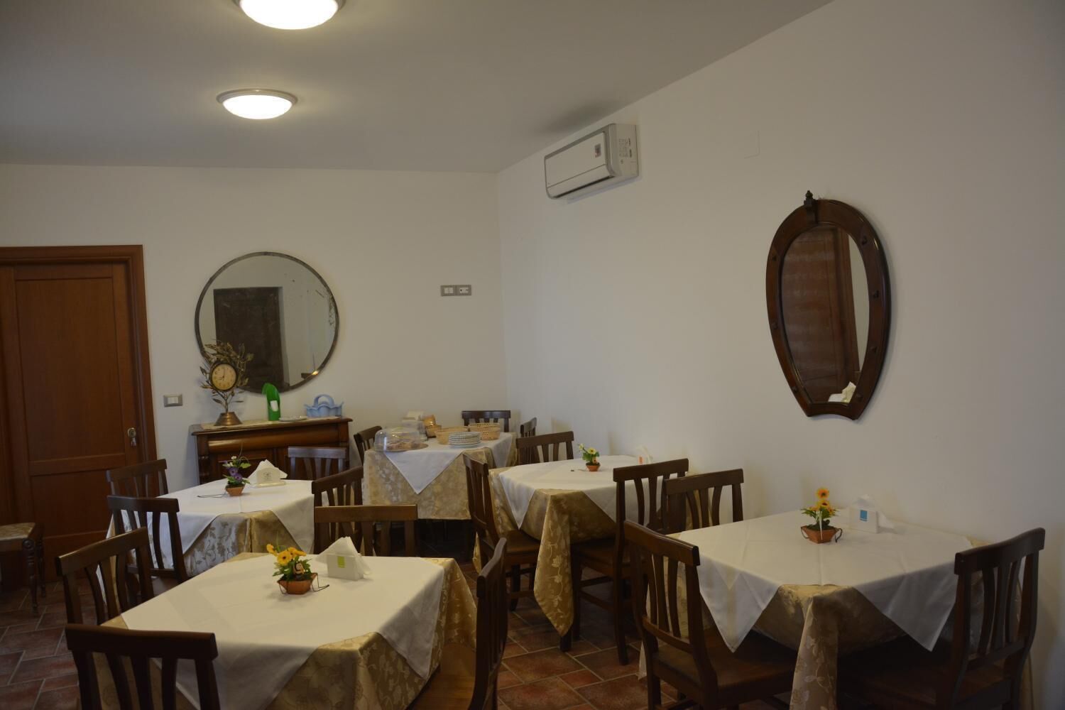 Un comedor con varias mesas cubiertas con manteles blancos, sillas de madera y un espejo grande en la pared.