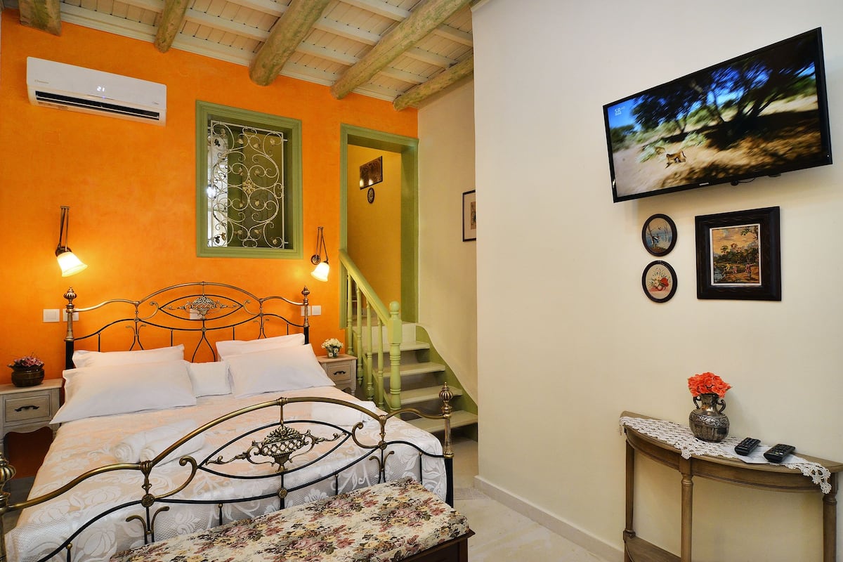 Une chambre à coucher comprenant un lit, une table de chevet, une commode, un escalier et un téléviseur fixé au mur.