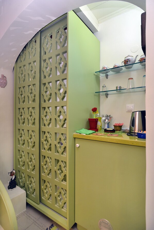 A kitchen with a green cabinet, a glass shelf with kitchenware, and a decorative partition.