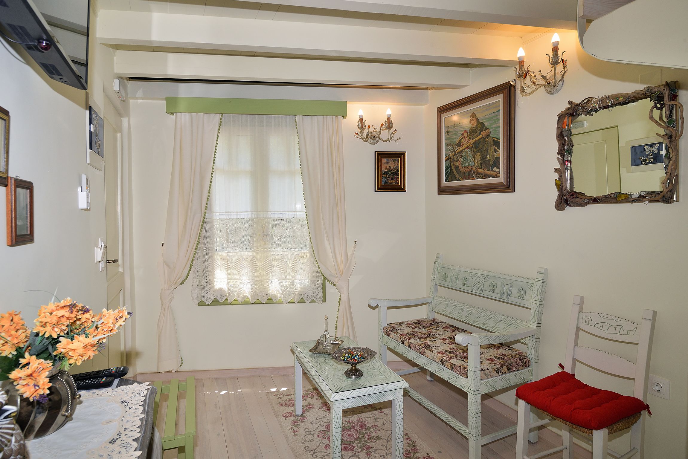 A room with a bed, a table with a vase of flowers, a chair with a red cushion, and a wall-mounted mirror.