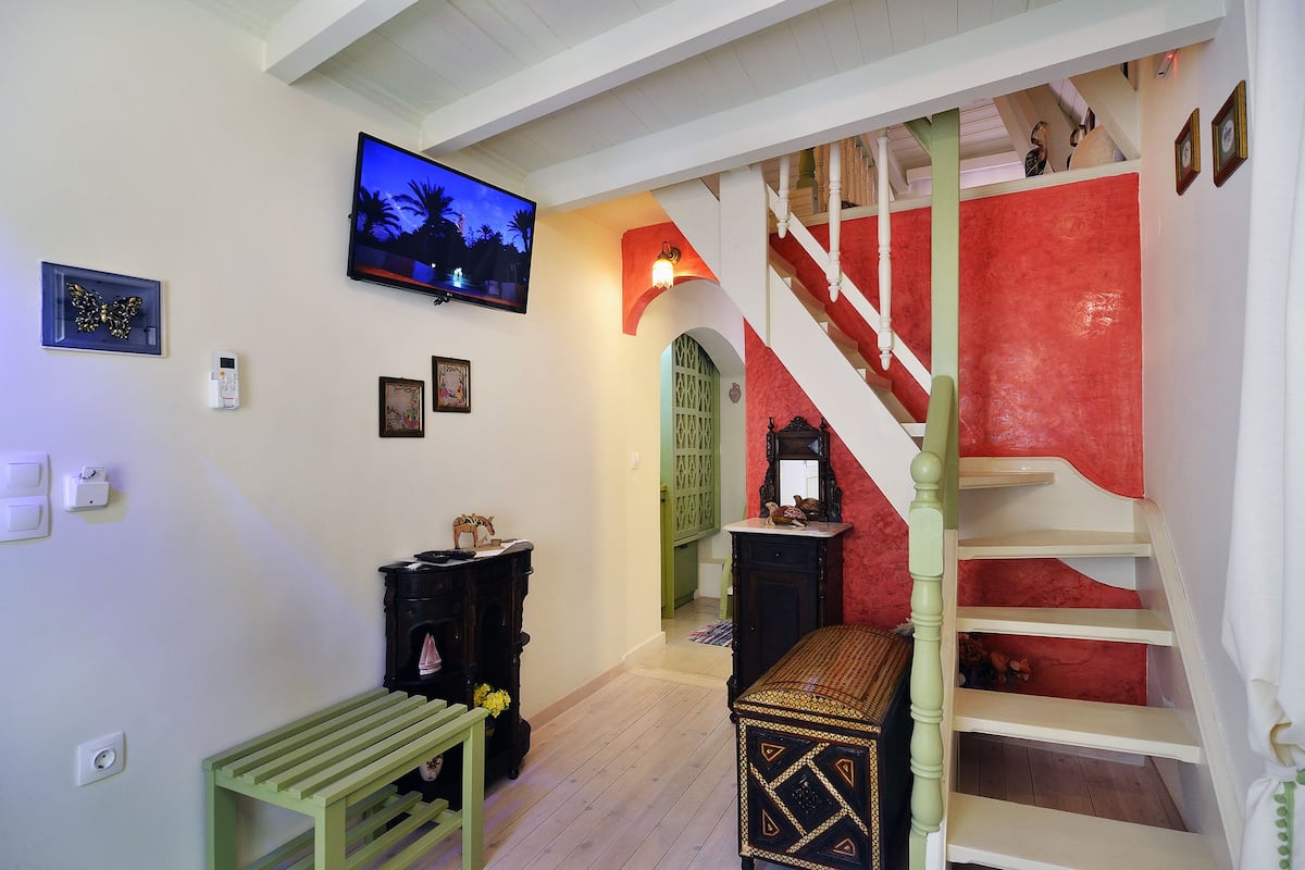 Un escalier avec un mur rouge, un banc en bois et un téléviseur fixé au mur.