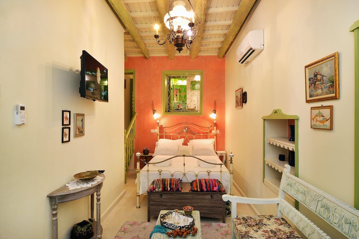 Une chambre à coucher comprenant un lit, des tables de chevet, une chaise, une petite table avec un plateau, et une fenêtre dotée d’un cadre vert.