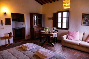 A cozy living room with a sofa, a dining table, and a kitchen area with wooden cabinets. - Bio-Agriturismo La Ginestra (San Casciano in Val di Pesa)