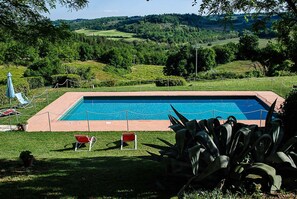 A rectangular swimming pool with a surrounding fence, two red lounge chairs, and a potted plant in the foreground. - Bio-Agriturismo La Ginestra (San Casciano in Val di Pesa)