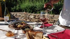 Mesa al aire libre con una botella de vino, una copa de vino, pan y un recipiente con miel.