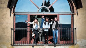 Un grupo de personas en un balcón con un amplio ventanal de arco que da a un paisaje pintoresco.