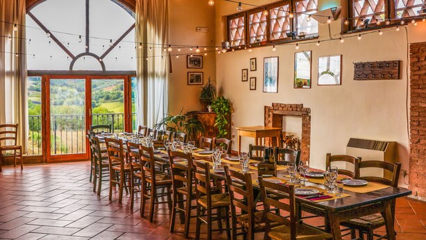 Un comedor con mesas y sillas de madera, una chimenea y un amplio ventanal de arco que da a un paisaje pintoresco.