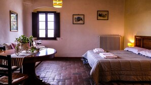 Una habitación acogedora con una mesa de madera, una cama con colcha, un radiador y una ventana con contraventanas.