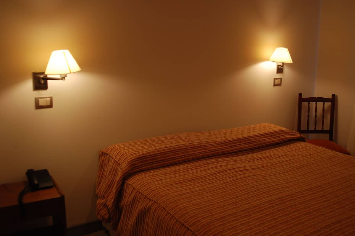 A hotel room with a bed, two wall-mounted lamps, a nightstand, and a chair.