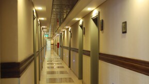 A long, well-lit hotel corridor with a checkered floor, doors on both sides, and a visible fire extinguisher. - Hotel Savoia Mendoza (Guaymallen)