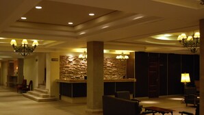 A lobby with a reception desk, stone wall, and seating area. - Hotel Savoia Mendoza (Guaymallen)