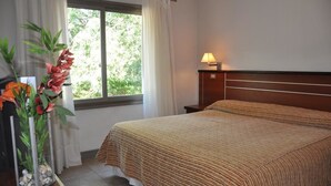 A neatly made bed with a striped bedspread, a bedside lamp, and a window with curtains. - Hotel Savoia Mendoza (Guaymallen)