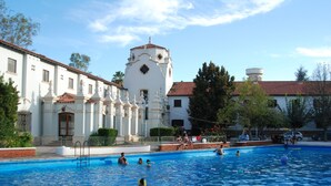 A swimming pool with people, a white building with a tower, and trees. - Hotel Savoia Mendoza (Guaymallen)