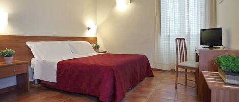 A hotel room with a bed, bedside tables, a desk with a chair, a television, and a window with curtains.