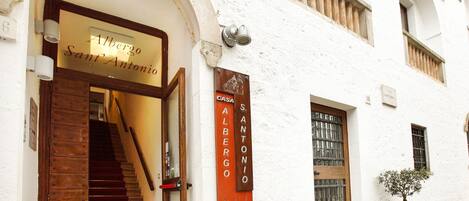 A building entrance with a wooden staircase, a sign reading "Albergo Sant'Antonio," and a smaller sign indicating "Casa Albergo."