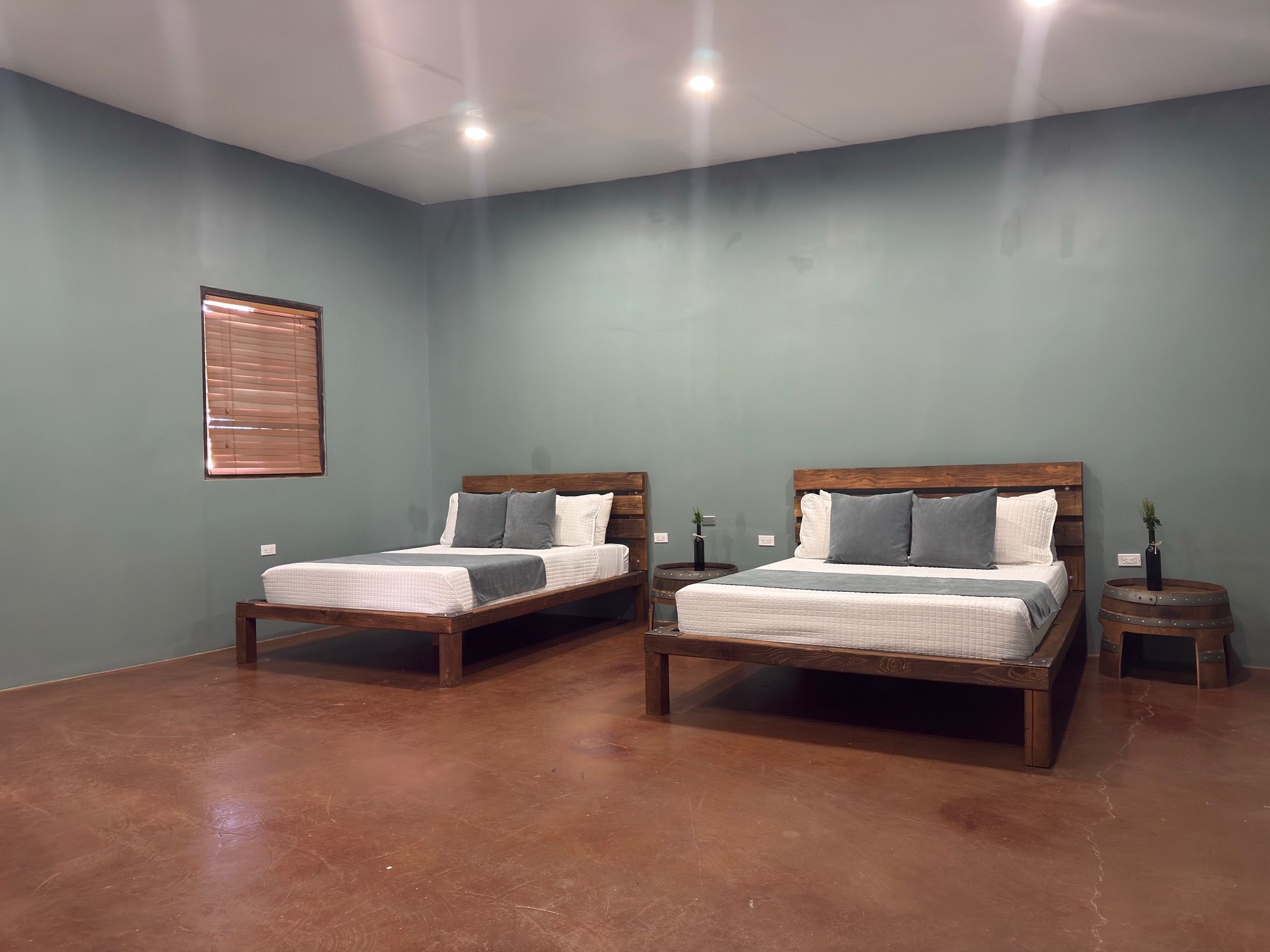 A room with two wooden beds, a small round table, and a wall-mounted light fixture.