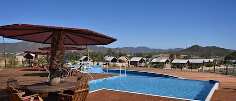 A pool area with wooden deck, lounge chairs, and umbrellas.