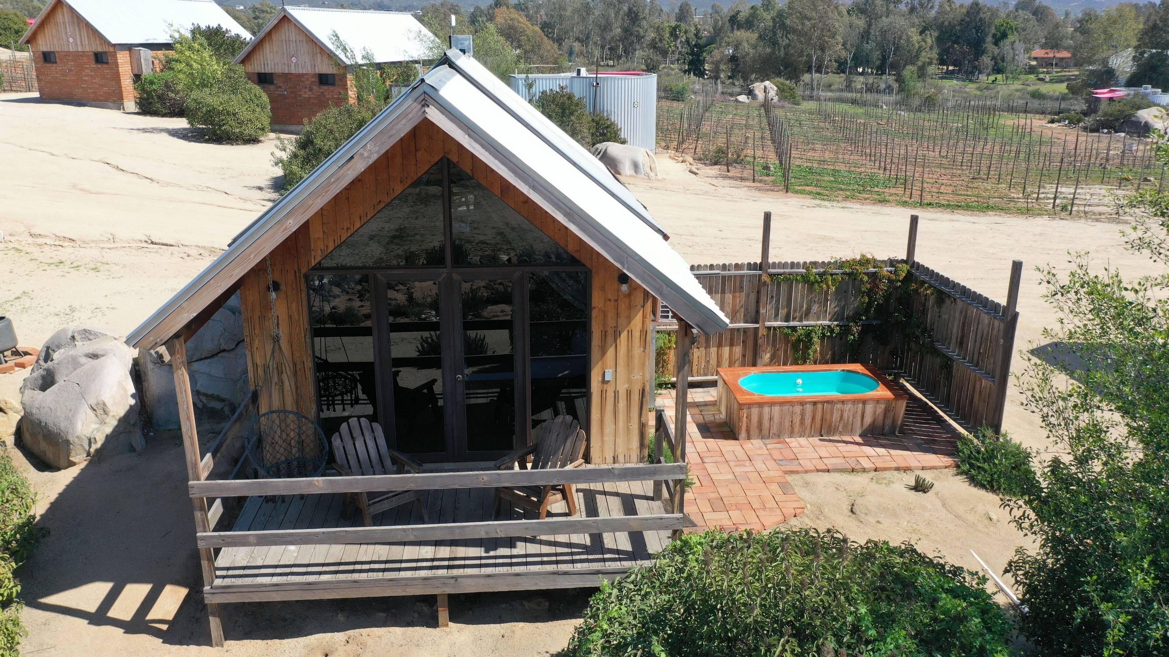 Una cabaña de madera con techo inclinado, un patio con terraza de madera y una piscina pequeña.