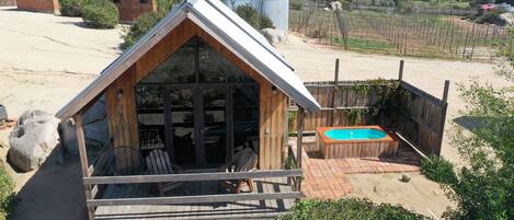 Una cabaña de madera con techo inclinado, un patio con terraza de madera y una piscina pequeña.