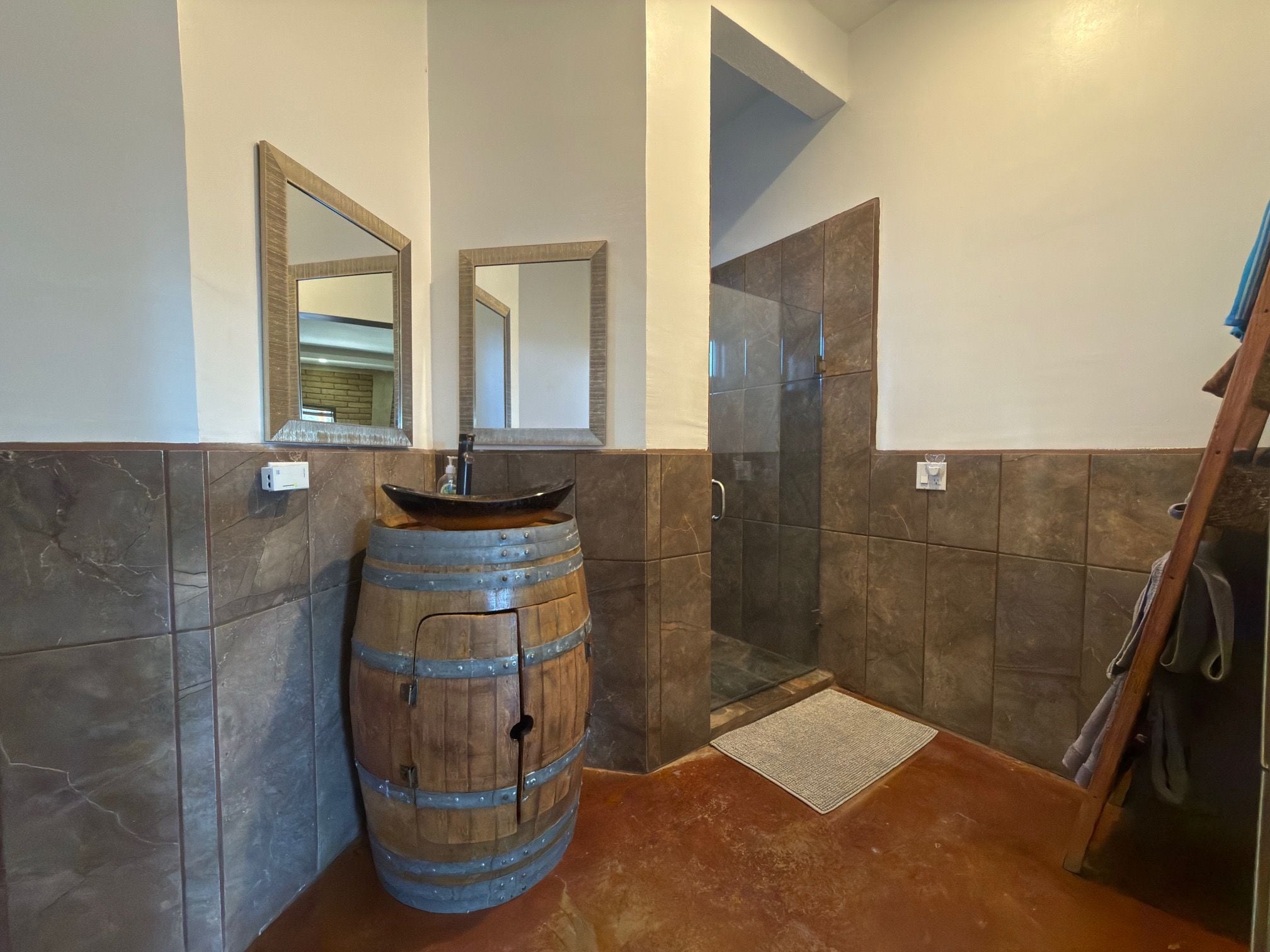 Un baño con un lavamanos de barril de madera, dos espejos y zona de ducha.