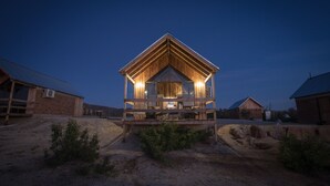 A wooden cabin with a balcony, surrounded by other cabins and a dirt ground. - Don Tomas Viñedo Cabañas (Valle de Guadalupe)