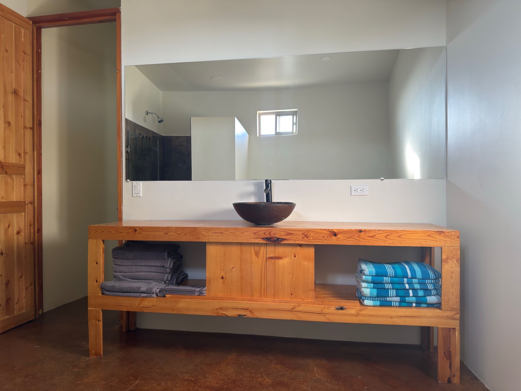 Un tocador de madera con un espejo grande, un lavabo y repisas para toallas.