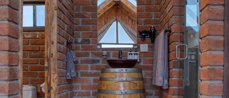 A rustic bathroom with a wooden barrel sink, a glass shower, and a brick wall.