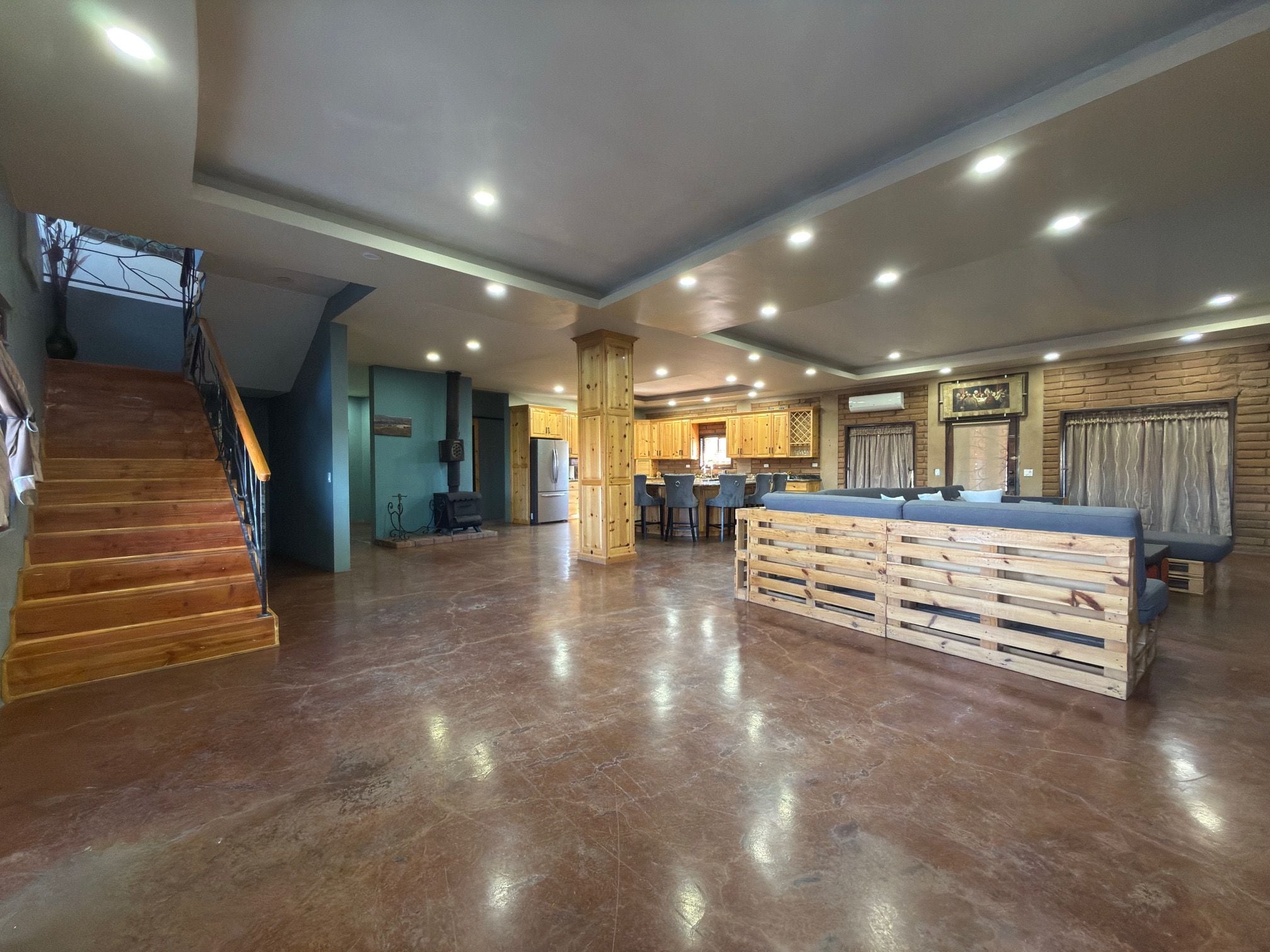 Un amplio salón con escalera de madera, cocina con armarios de madera y zona de bar.