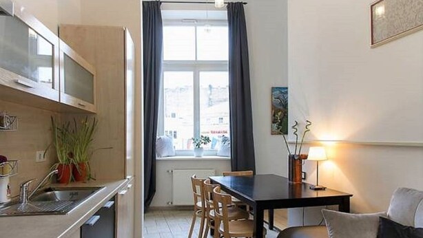 A compact kitchen with a dining area, a window with curtains, and a lamp on the table. - 2 Bedroom Apartment near Town Hall (Vilnius)