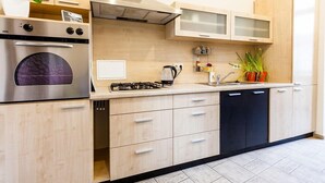 A modern kitchen with a built-in oven, stove, and dishwasher, featuring light wood cabinets and a black dishwasher. - 2 Bedroom Apartment near Town Hall (Vilnius)