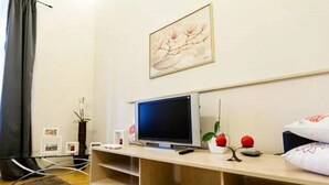 A modern living room with a flat-screen TV on a wooden stand, a framed artwork above the TV, and a cozy seating area with a rug and cushions. - 2 Bedroom Apartment near Town Hall (Vilnius)