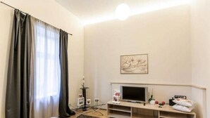 A modern hotel room with a bed, a TV, a small table, and a window with curtains. - 2 Bedroom Apartment near Town Hall (Vilnius)