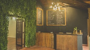 Ein Restaurantinneres mit einem hölzernen Empfangstresen, einer Kreidetafel mit Speisekarte und einer grünen, blättrigen Wand.