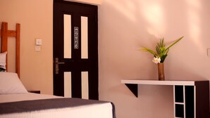 Ein Hotelzimmer mit einem Bett, einer Tür mit einem Schild, einem kleinen Regal mit einer Vase und einer Wandleuchte.