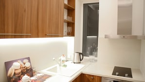 A modern kitchen with wooden cabinets, a stainless steel kettle, and a digital clock displaying 1:38. - Brand New Labdariu Str Apartment (Vilnius)
