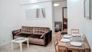 A living room with a brown sofa, a white coffee table, and a dining area with a wooden table set for four. - Brand New Labdariu Str Apartment (Vilnius)