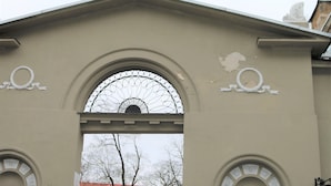 A building entrance with a large arched doorway, a statue on top, and a sign for 'Narvesen' store. - Brand New Labdariu Str Apartment (Vilnius)