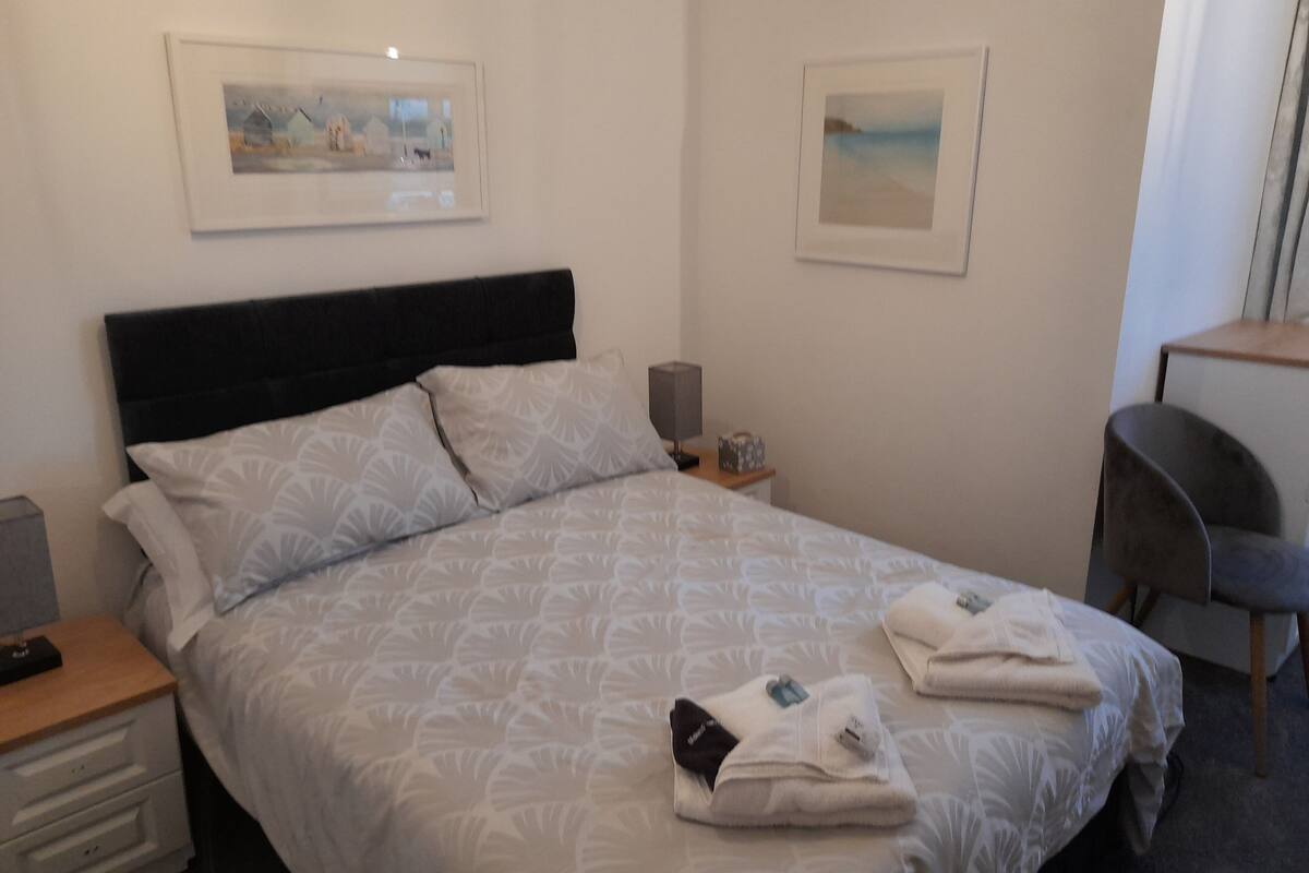 A hotel room with a bed, two bedside tables, a desk, and two framed pictures on the wall.
