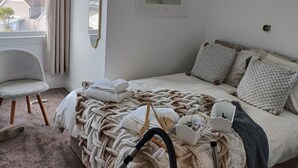 A bedroom with a bed, a chair, a vacuum cleaner, and a window with curtains.