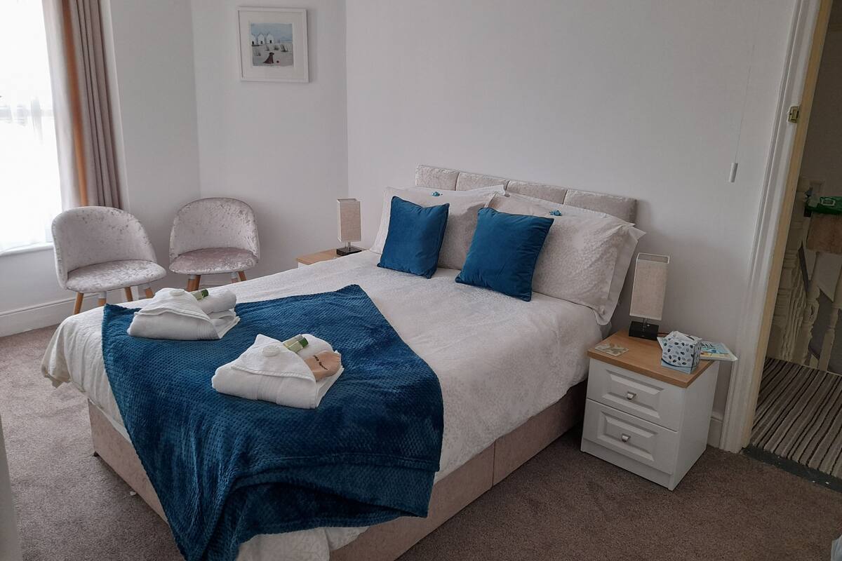 A neatly arranged bedroom with a large bed, two chairs, a bedside table, and a small bedside lamp.