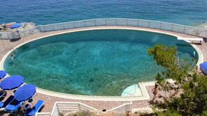 Piscina azul cristalina con cubierta de piedra, rodeada por una barandilla metálica y equipada con sombrillas azules.