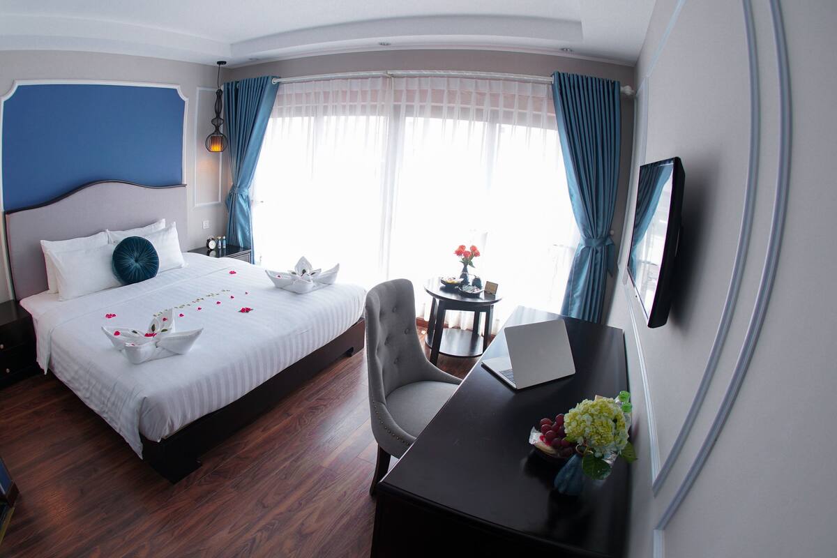 Une chambre d’hôtel comprenant un lit, un bureau avec un ordinateur portable, une chaise, une table de chevet avec une lampe et une fenêtre avec des rideaux.