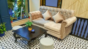 Una habitación con un sofá capitonado, un reposapiés redondo, una mesa de centro de madera oscura y baldosas de suelo con diseño.