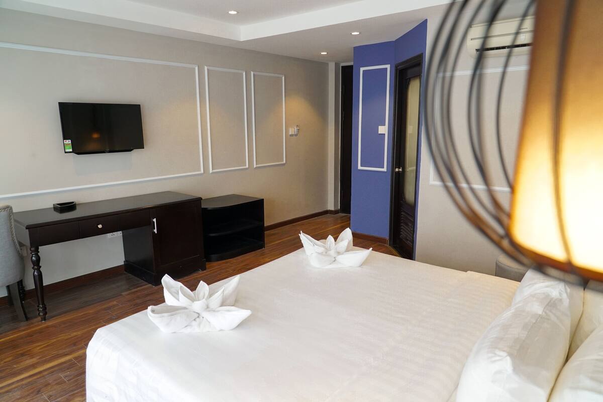 Une chambre d’hôtel avec un lit, un bureau, une chaise et un téléviseur fixé au mur.