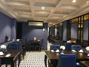 A hotel dining area with a patterned floor, dark blue upholstered chairs, and tables set with white flowers. - Hanoi La Castela Hotel (Hanoi)
