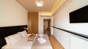 Een hotelkamer met twee bedden, een aan de muur bevestigde televisie en een houten garderobe.
